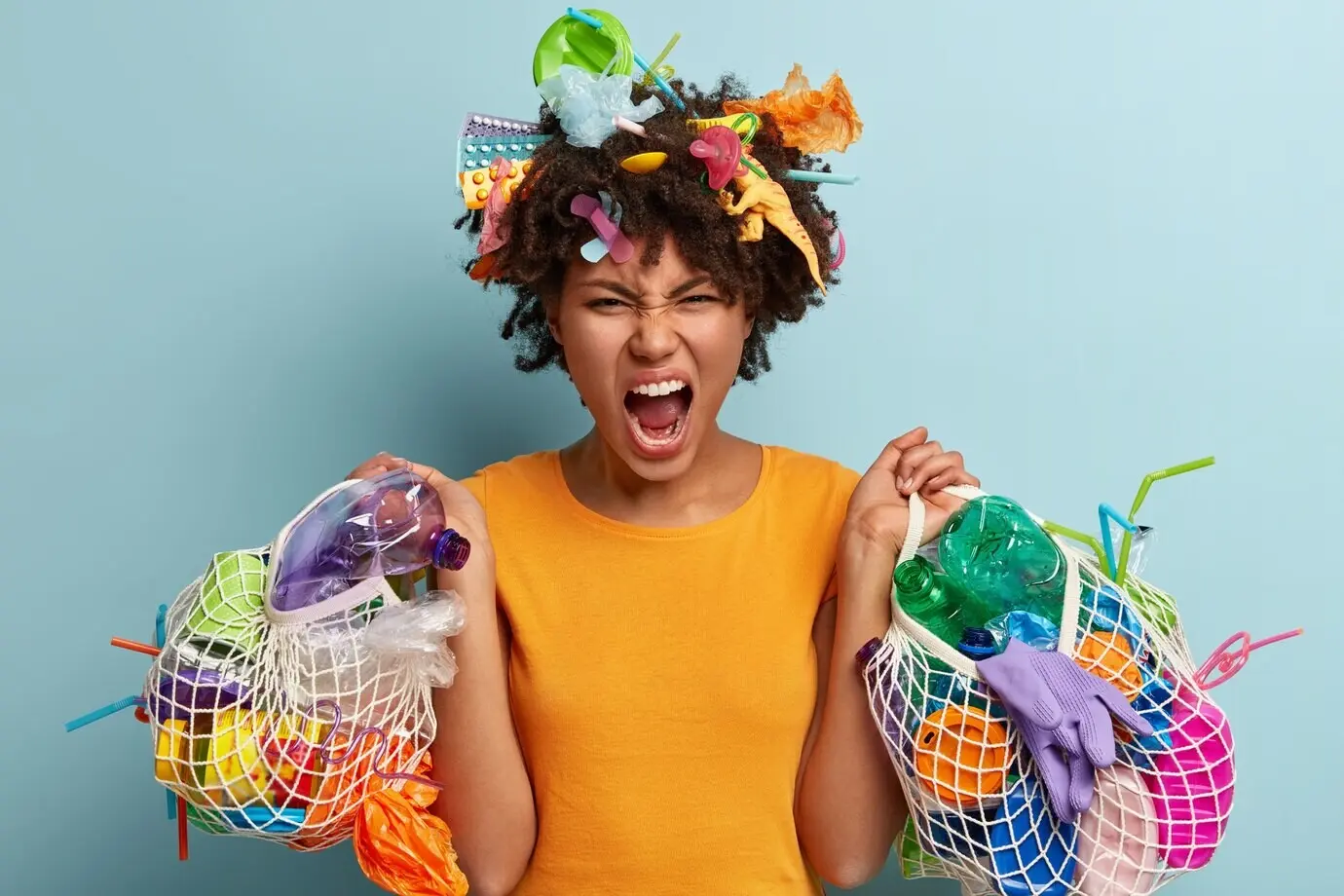 Gereizte junge schwarze Frau sammelt Plastikmüll, hält den Mund geöffnet, hält Netzbeutel mit Müll, zeigt negative Emotionen, fordert, die Natur zu retten, recycelt Müll. Umweltproblem.