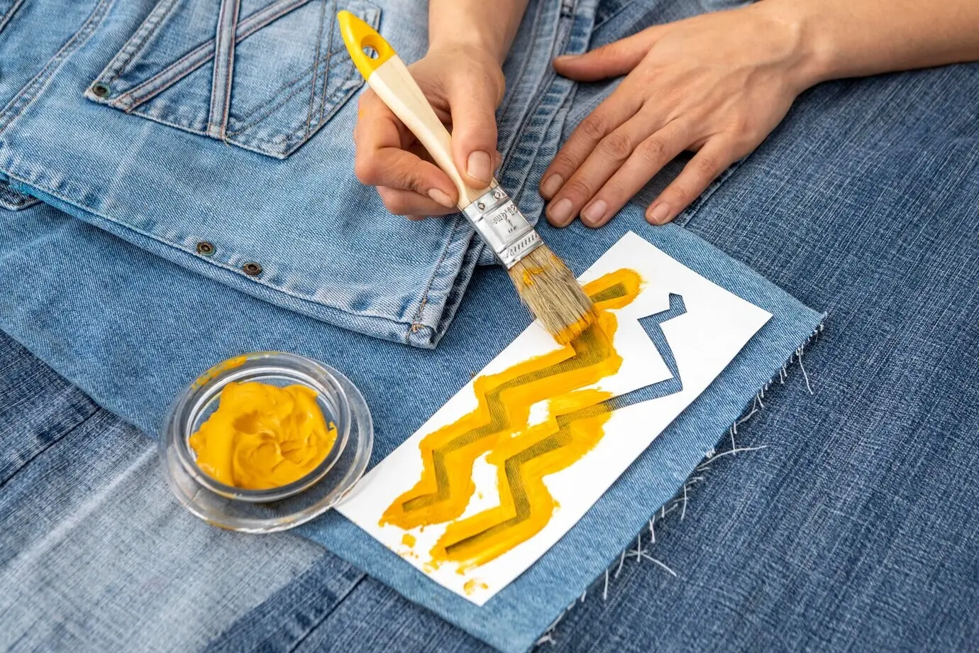 Nahaufnahme einer Hand beim Bemalen von Jeans.